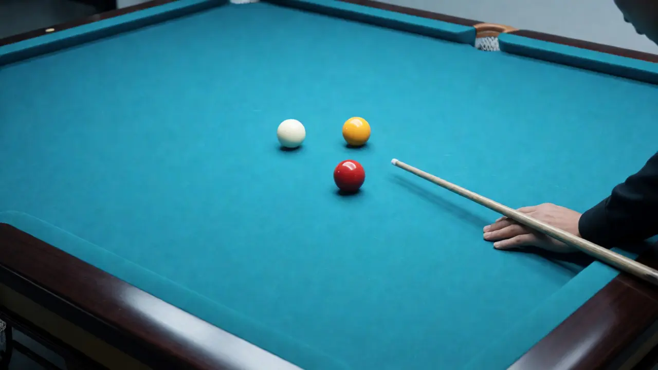 Hráč míří tyčí na tři koule na velkém kulečníkovém stole bez kapes.